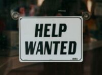 white sign with black type, saying Help Wanted