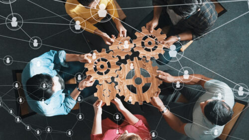 overhead view of seated people fitting together 5 wooden cogs of different sizes