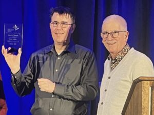 Brett Bobley holding a clear award plaque (left) and Peter Berkery