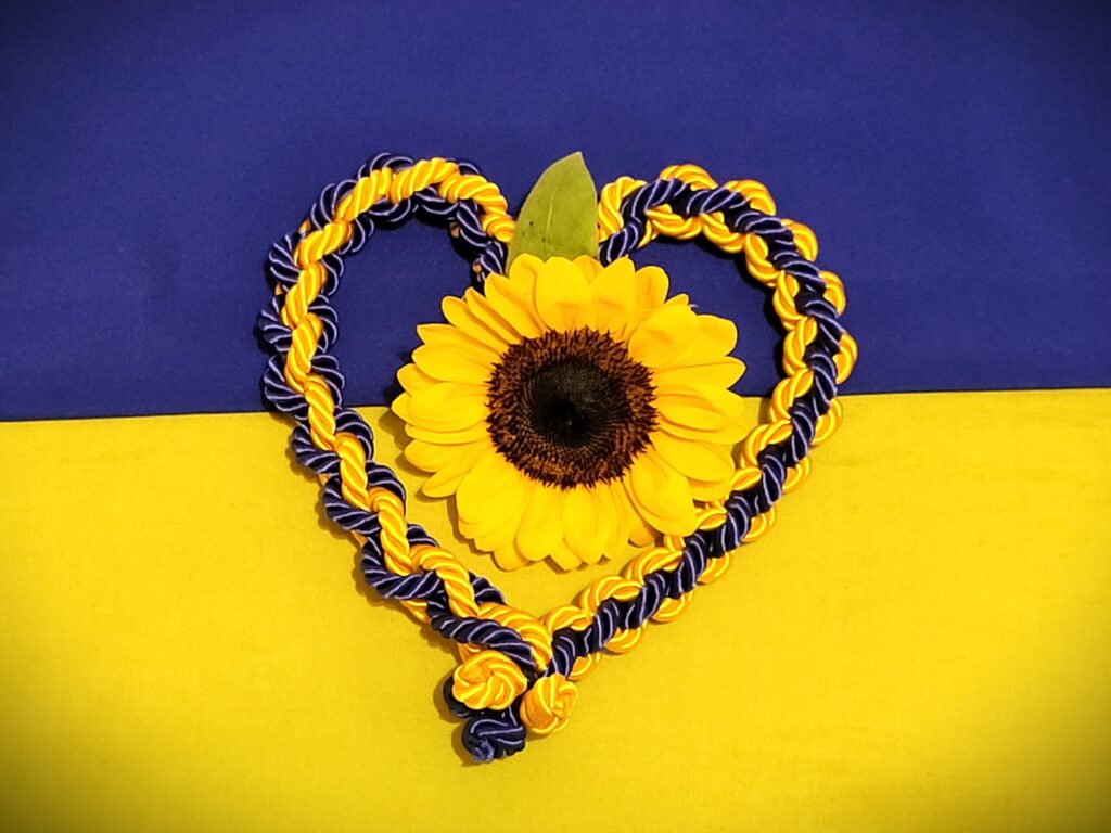 Braided yellow and blue ribbons in the shape of a heart, with a sunflower in the center, arranged on top of a yellow and blue flag